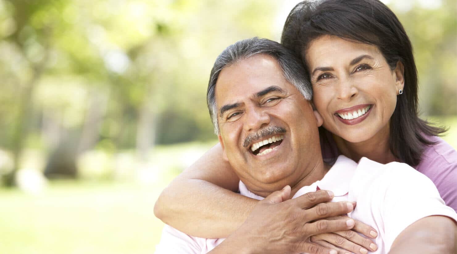 Two senior citizen couple smile at the camera while holding each other.